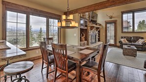 Un comedor amplio con una gran mesa de madera y sillas, una araña y ventanas grandes que ofrecen vistas del paisaje circundante.