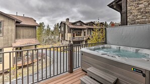 Un jacuzzi en una terraza de madera con un muro de piedra y vistas a casas vecinas.