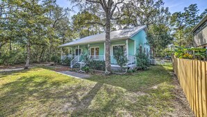 A single-story house with a porch, surrounded by a wooden fence and trees. - Oak Island Home w/ Yard < 1 Mi to the Beach! (Oak Island)