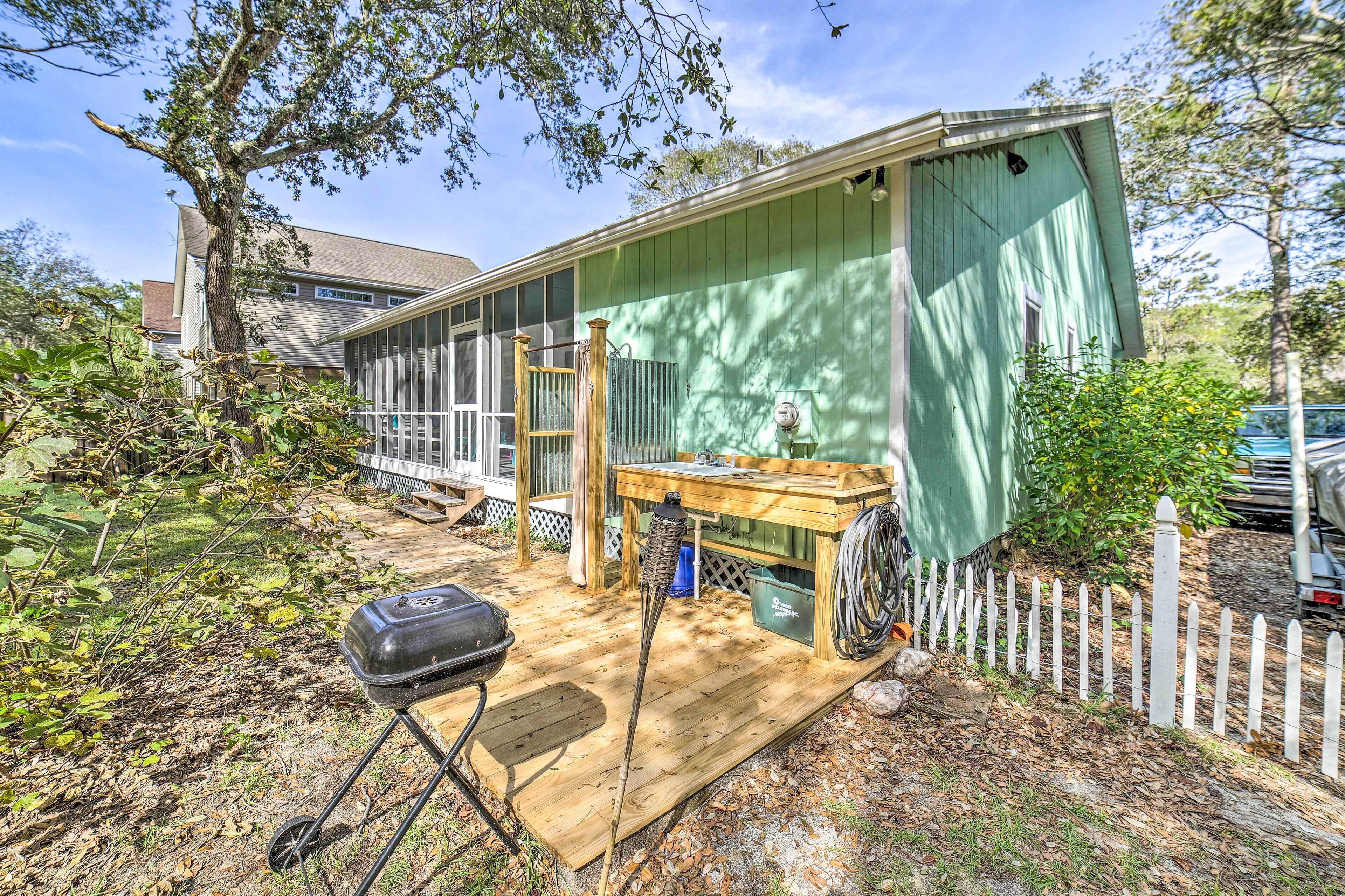 A green building with a wooden deck, a table, and a grill.
