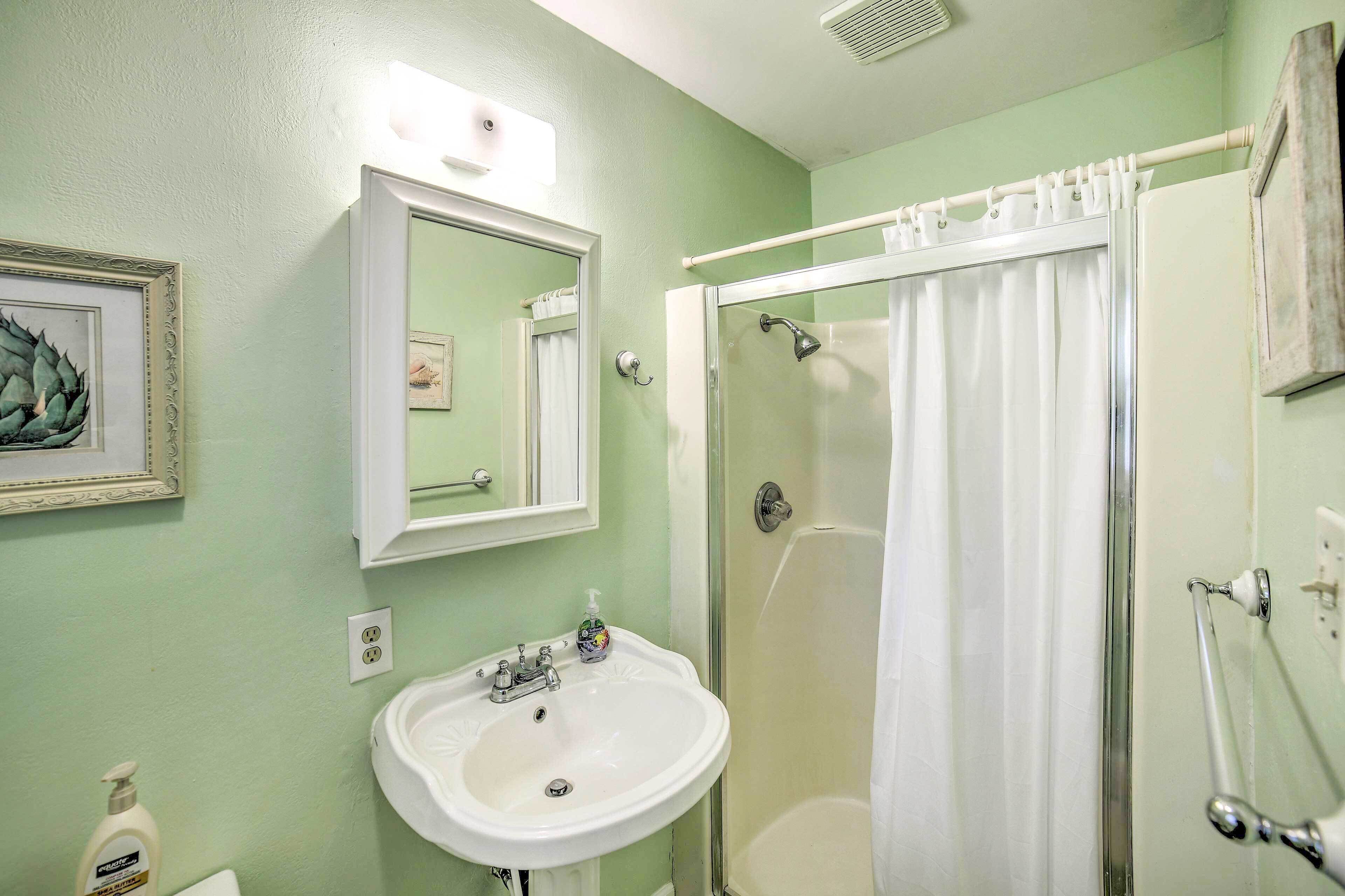 Une salle de bain avec un lavabo, un miroir, une douche et un tableau encadré au mur.