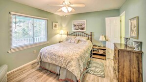 A bedroom with a bed, a ceiling fan, a nightstand, a dresser, a window with blinds, and a door. - Oak Island Home w/ Yard < 1 Mi to the Beach! (Oak Island)