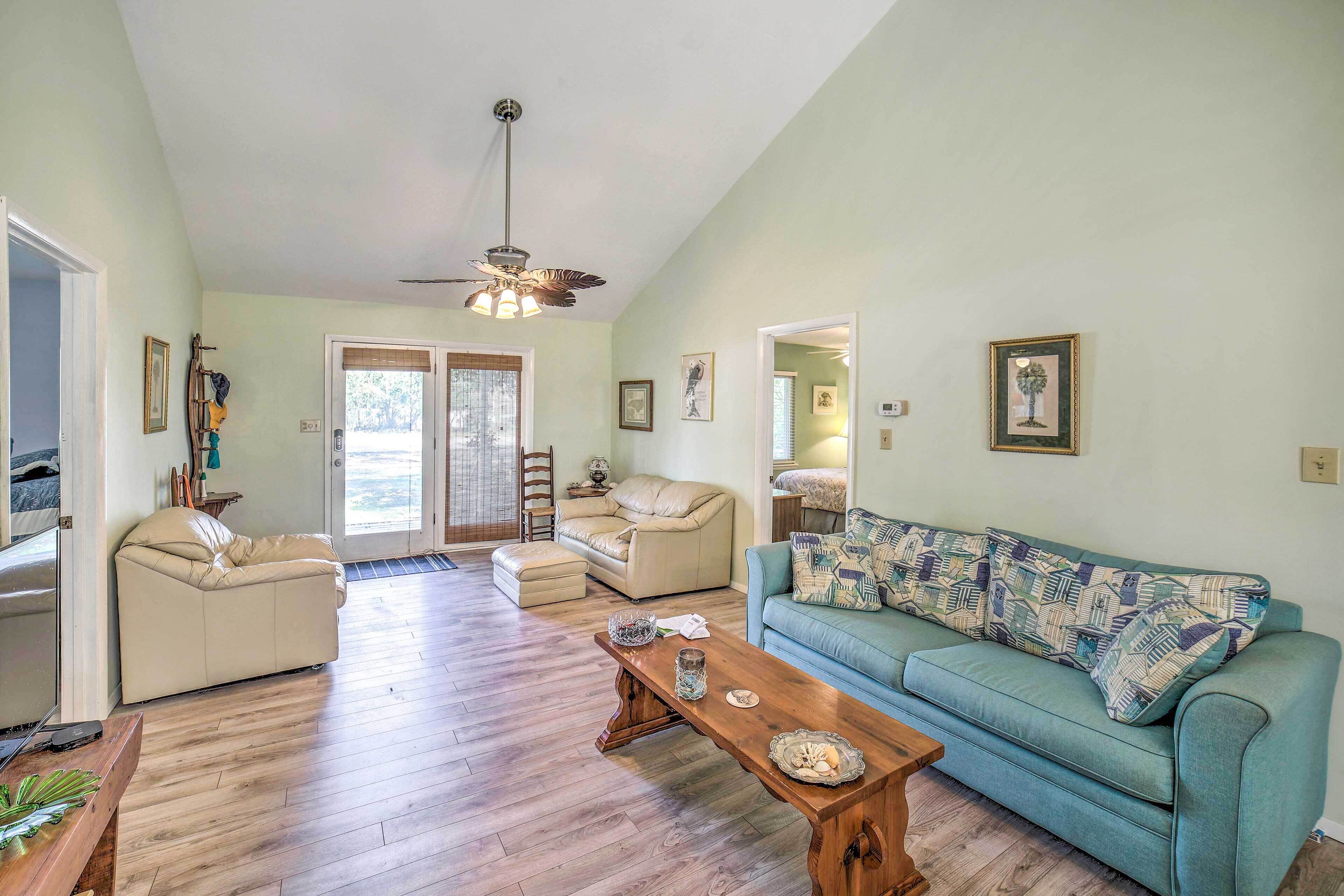 A spacious living room with a wooden floor, a blue sofa, a beige sofa, a wooden coffee table, and a ceiling fan.