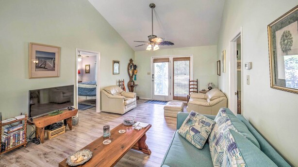 A spacious living room with a wooden coffee table, a sofa, and a TV. There are two doors leading to other rooms. - Oak Island Home w/ Yard < 1 Mi to the Beach! (Oak Island)