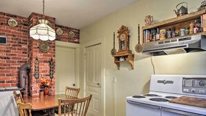 Een keuken met een bakstenen muur, een witte oven, houten stoelen en een hangende lamp.