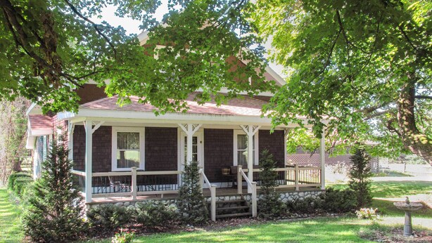 Een tweelaags huis met een overdekte veranda, een stenen fundering en een verzorgd gazon.