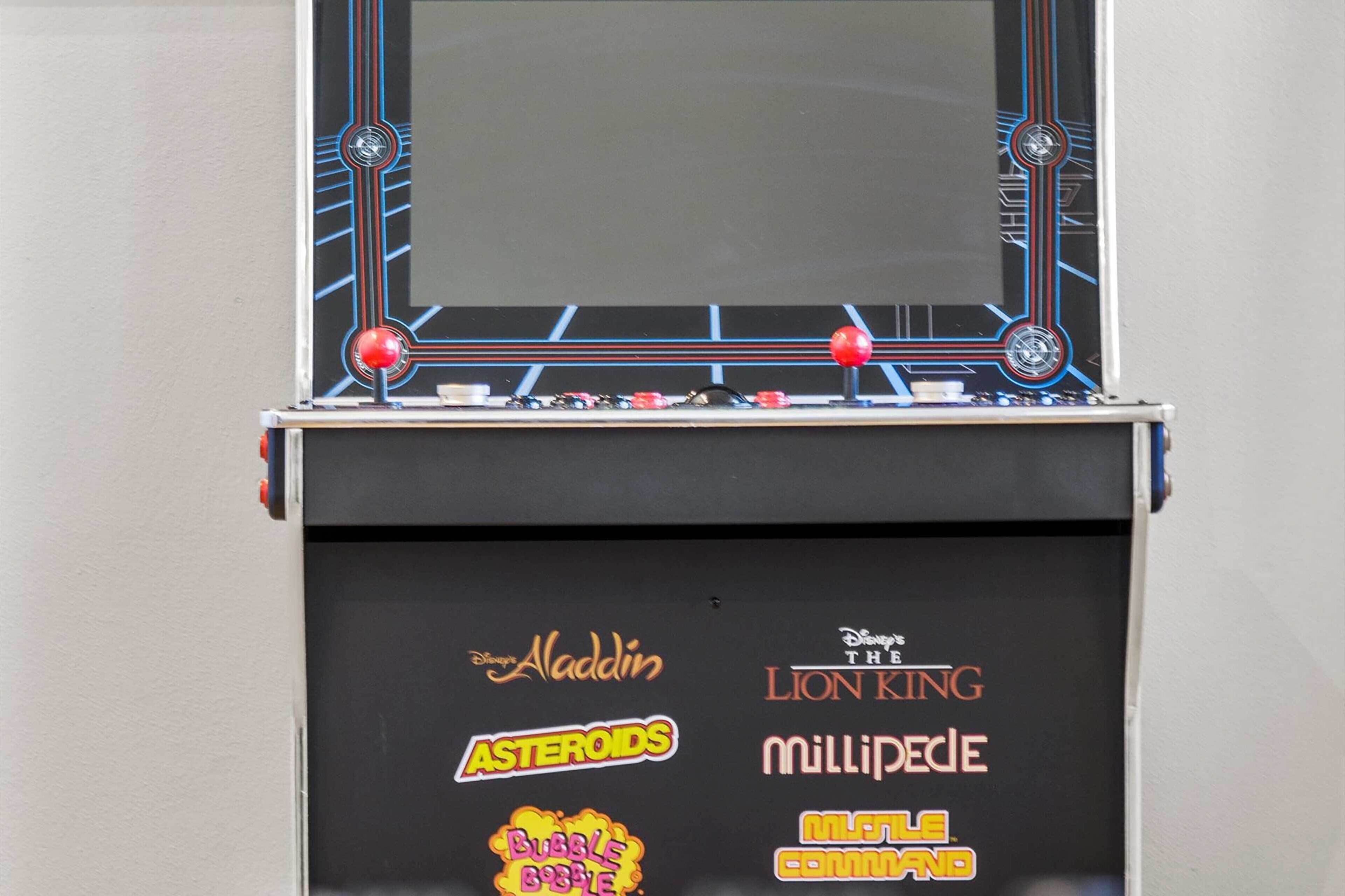 A vintage arcade machine with a black base featuring stickers of various Disney movies like 'Aladdin,' 'Asteroids,' 'The Lion King,' 'Millipede,' and 'Bubble Buster.'