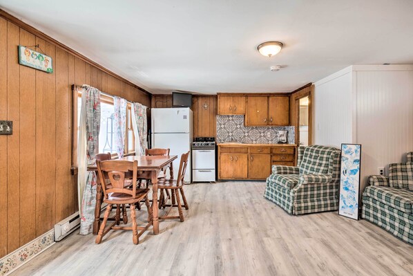 A compact kitchen with wooden cabinets, a refrigerator, a stove, and a dining table with chairs. - No-frills Hampton Cottage - Steps to Beach! (Hampton)