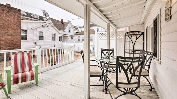 A covered porch with a table and chairs, a striped chair, and a white fence. - No-frills Hampton Cottage - Steps to Beach! (Hampton)