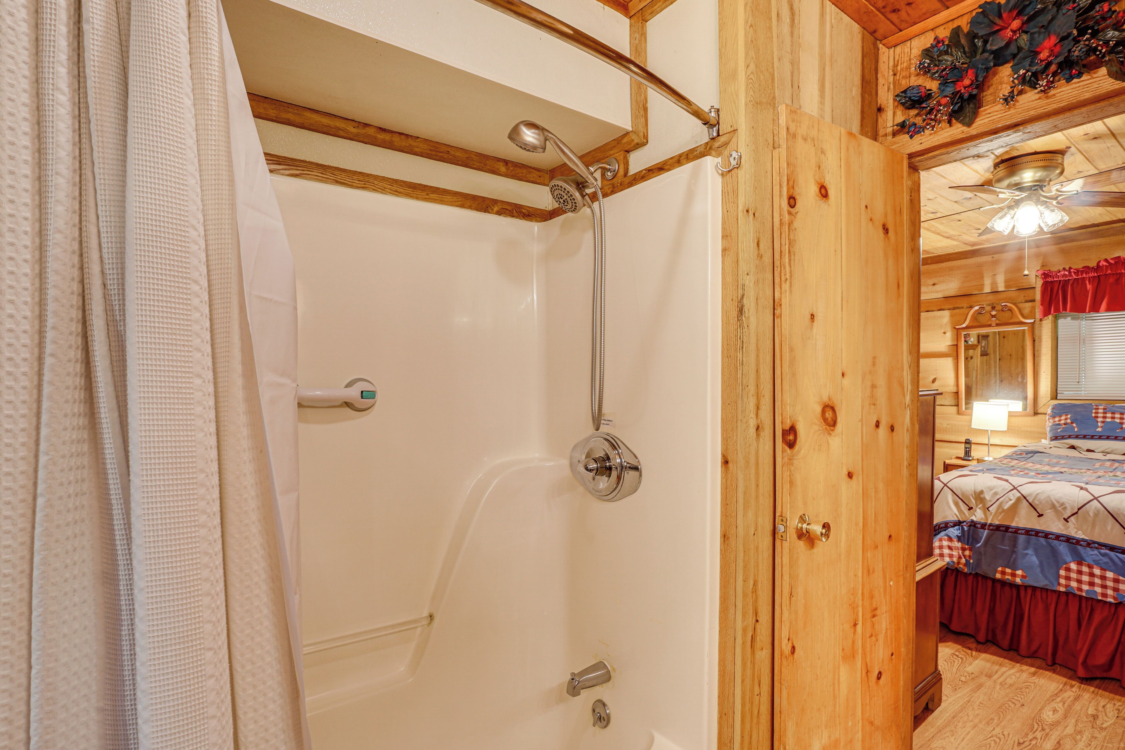 A wooden cabin interior with a shower, a bed with a red and blue checkered bedspread, and a wooden ceiling.