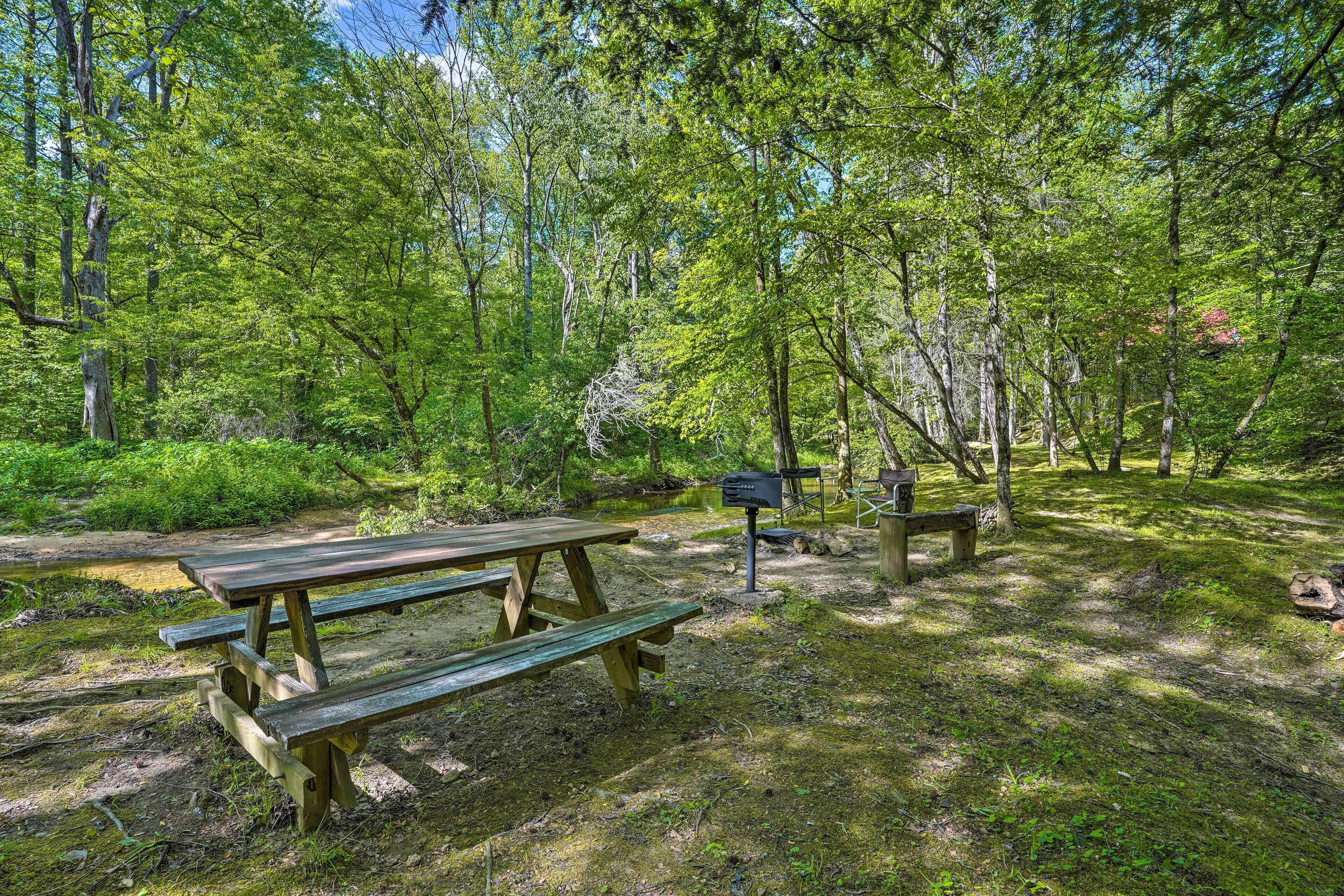 A picnic area with wooden benches and a grill station in a forested setting.