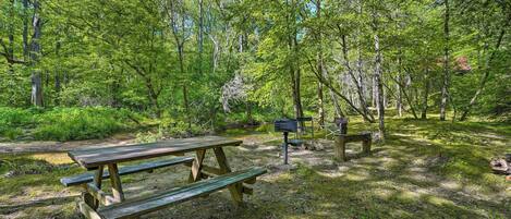 A picnic area with wooden benches and a grill station in a forested setting.