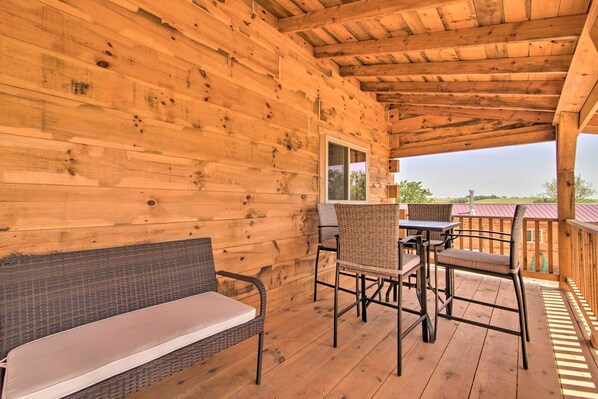Una terraza de madera con un banco y sillas, una mesa, y vistas del paisaje.