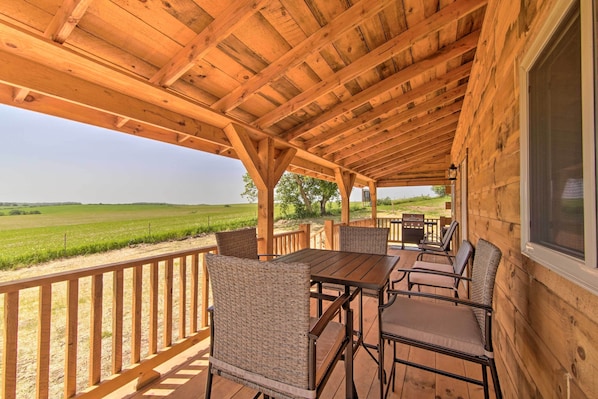 A wooden deck with a table and chairs, overlooking a green field.