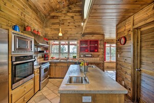 Cocina de cabaña de madera con electrodomésticos de acero inoxidable, una isla grande con un lavamanos y una ventana con marco rojo.