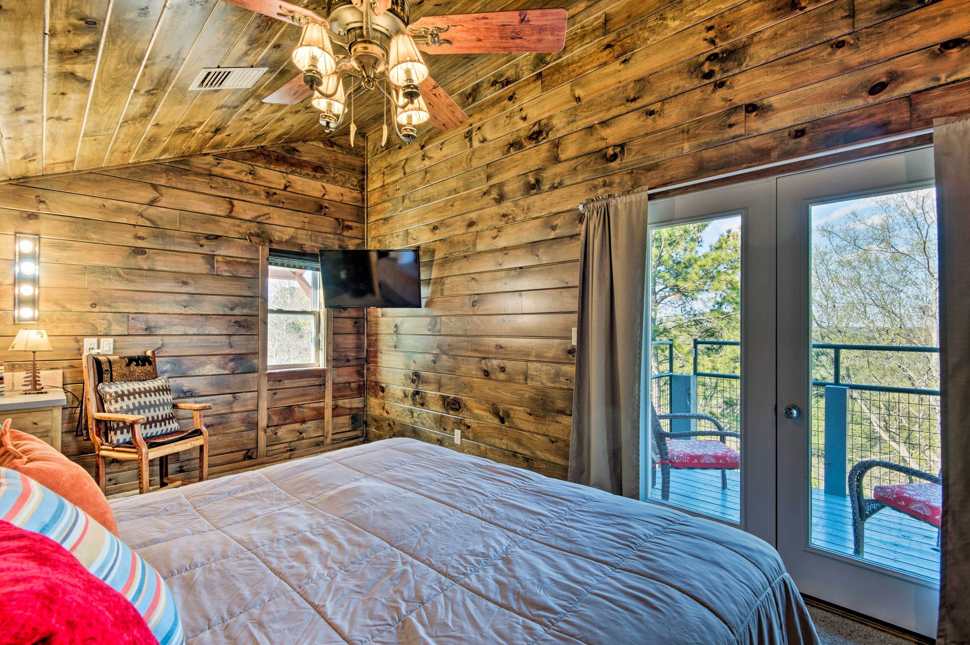 A wooden cabin bedroom with a bed, a chair, a TV, and a balcony with chairs.