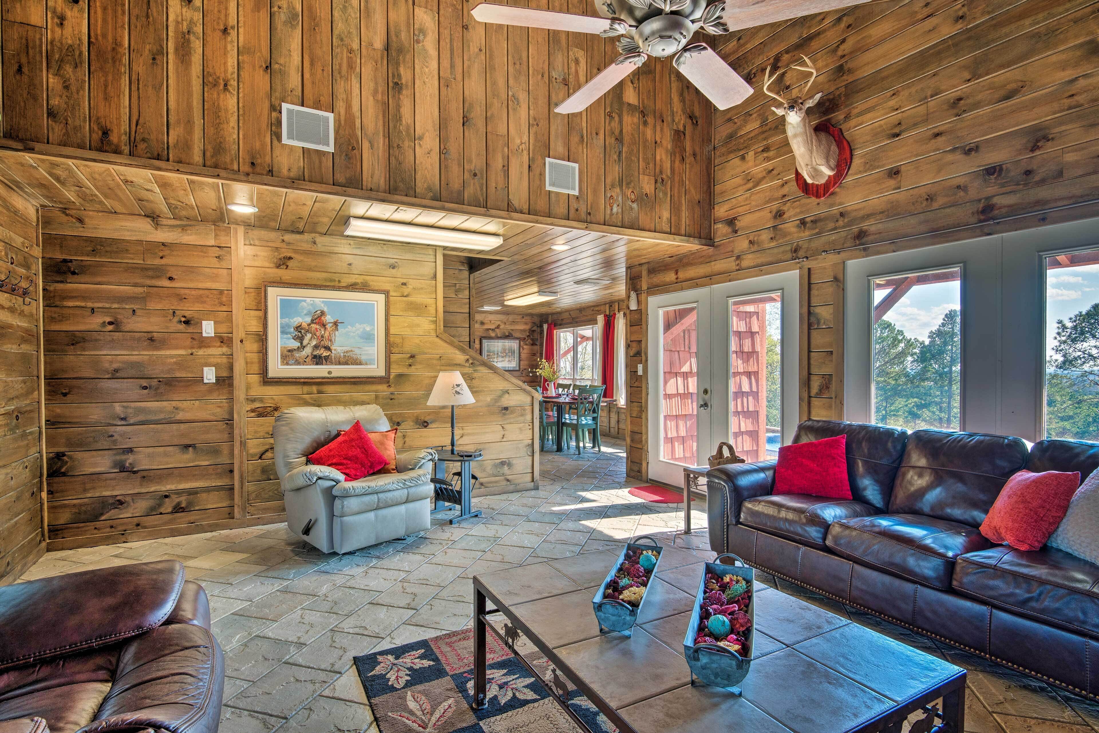 A log cabin interior with a leather sofa, a dining table, and a ceiling fan.