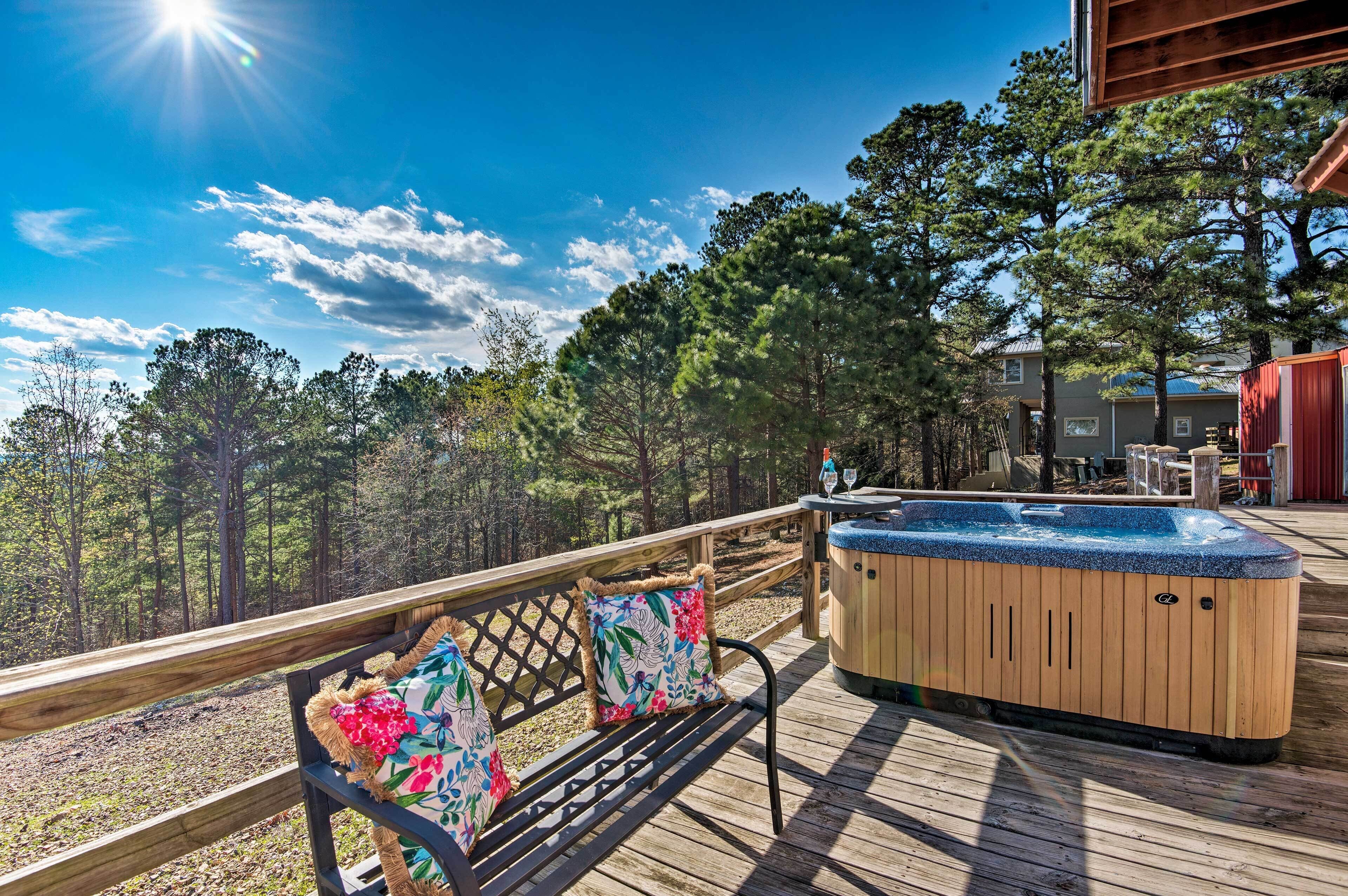 A wooden deck with a hot tub, a bench with floral cushions, and a view of a forested area.