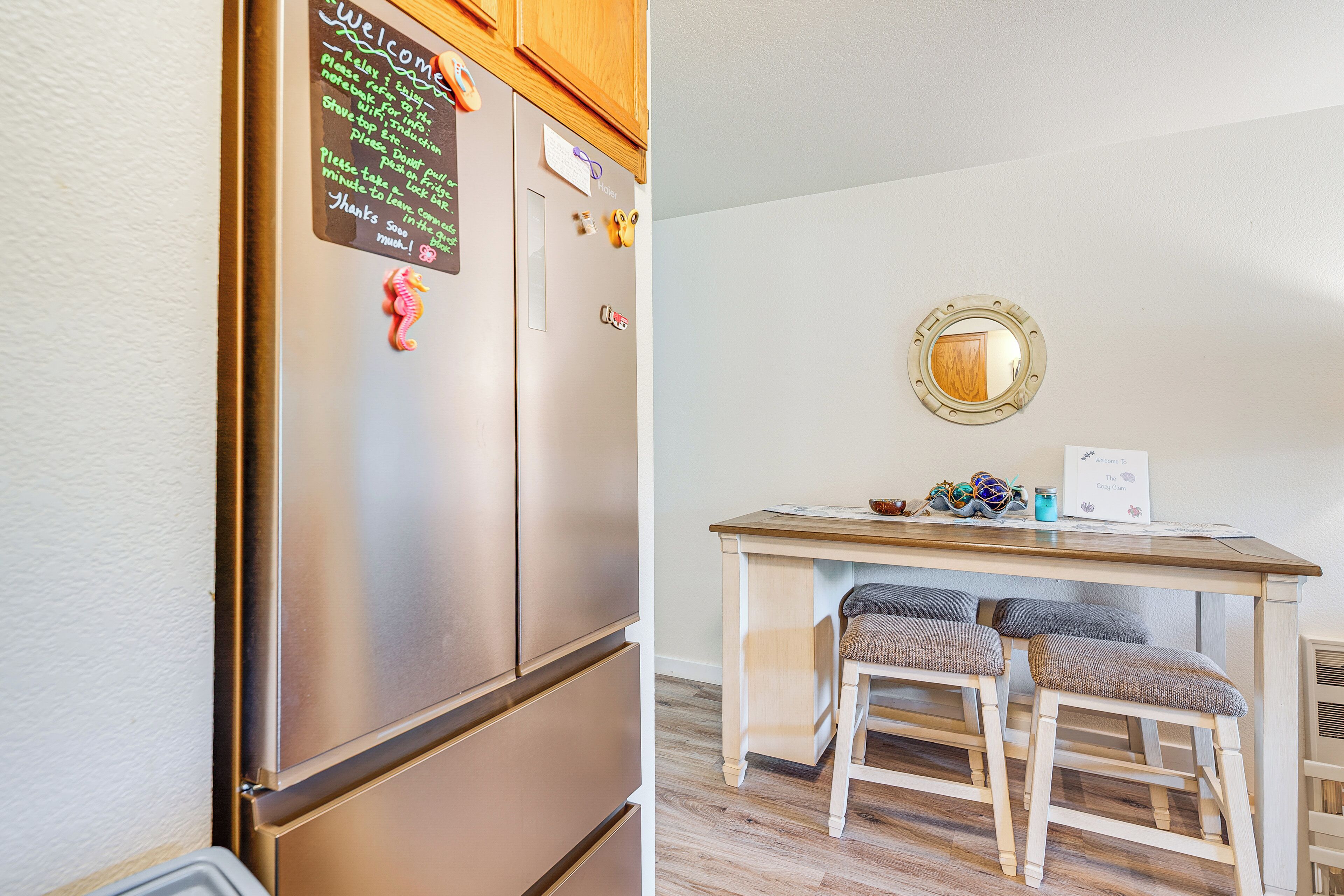 A kitchen with a stainless steel refrigerator, wooden cabinets, and a small dining table with two stools.