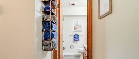 A hallway leading to a bathroom with a towel rack and a framed picture on the wall.