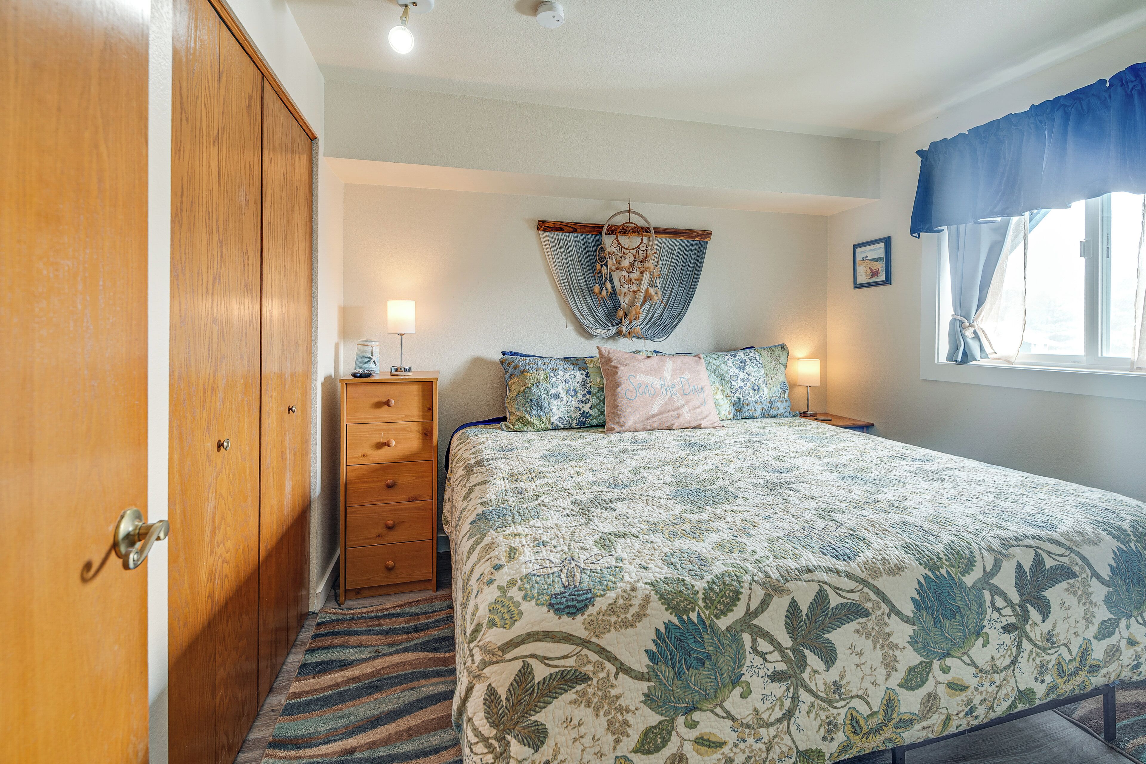 A bedroom with a bed, a dresser, a nightstand, a dreamcatcher, and a window with curtains.