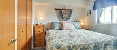 A bedroom with a bed, a dresser, a nightstand, a dreamcatcher, and a window with curtains.