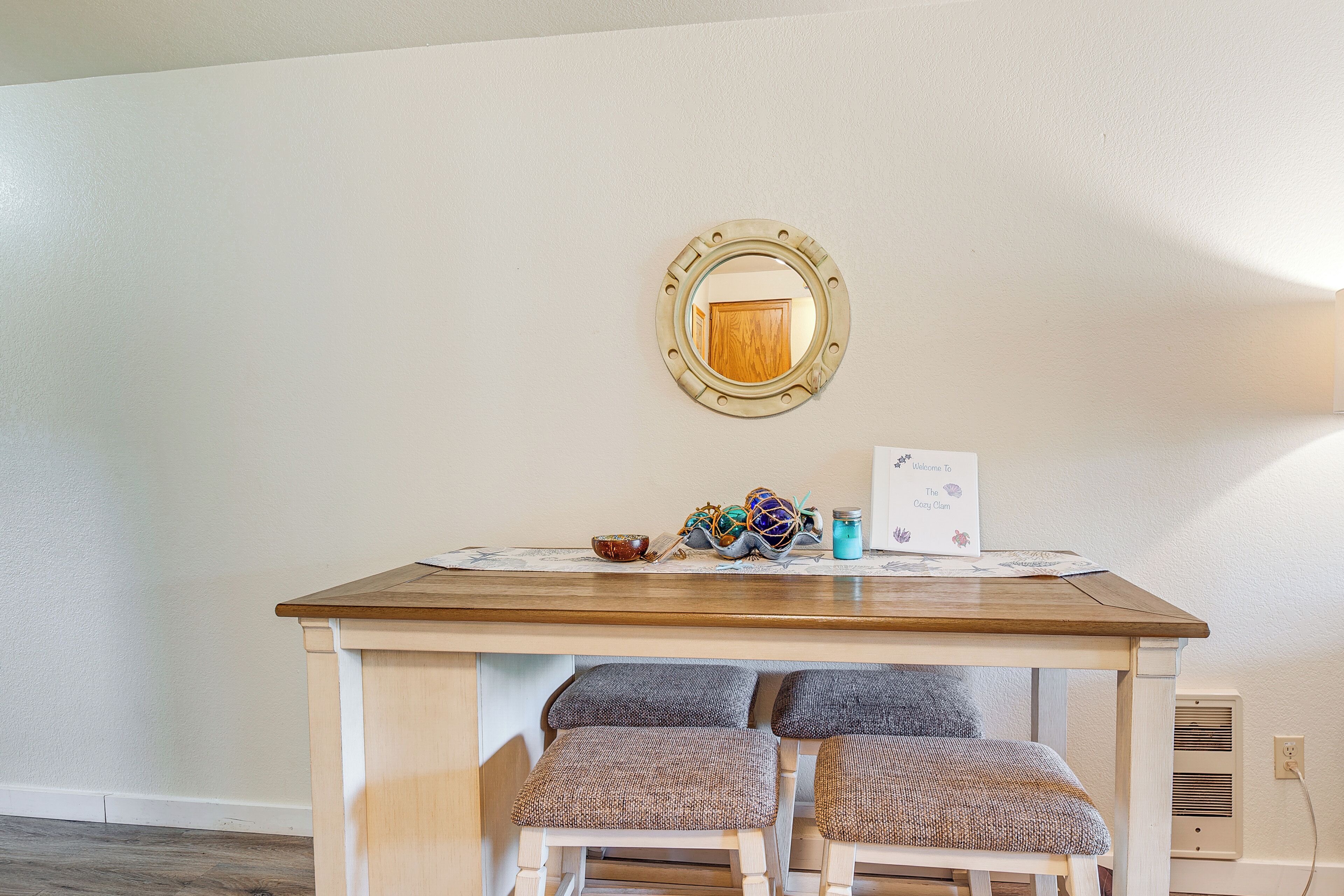 Een gezellig eetgedeelte met een houten tafel, twee comfortabele stoelen, een decoratieve spiegel en een welkomstbord.