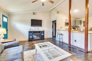 A living room with a sofa, coffee table, and a fireplace. There is a kitchen area with a bar and stools.