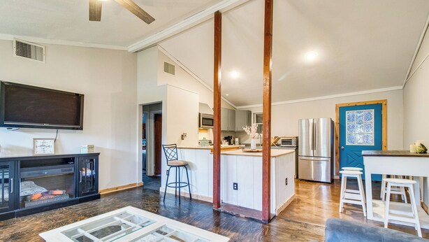 A spacious living area with a large TV, a glass coffee table, a blue sofa, and a kitchen with white cabinets and stainless steel appliances. - Arkansas Vacation Rental < 1 Mi to Norfork Lake (Mountain Home)