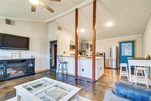 A spacious living area with a large TV, a glass coffee table, a blue sofa, and a kitchen with white cabinets and stainless steel appliances. - Arkansas Vacation Rental < 1 Mi to Norfork Lake (Mountain Home)