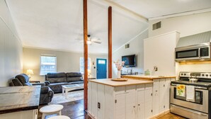 A compact kitchen with a central island, a dining area with stools, a sofa, and a TV in the background. - Arkansas Vacation Rental < 1 Mi to Norfork Lake (Mountain Home)