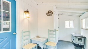 A room with a blue door, a small table with chairs, a wall-mounted light, and a trash bin. - Arkansas Vacation Rental < 1 Mi to Norfork Lake (Mountain Home)