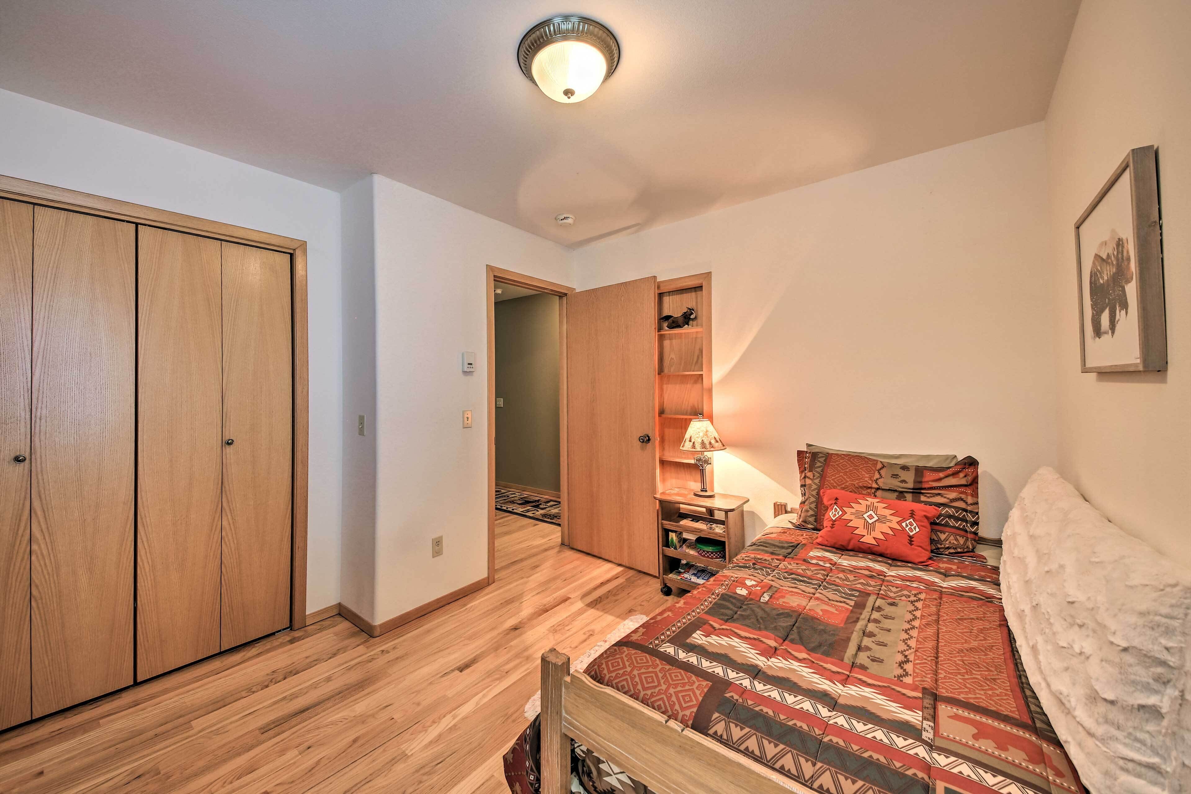 A bedroom with a wooden wardrobe, a bed with patterned bedding, a bedside table with a lamp, and a framed picture on the wall.