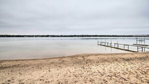 A beach with a wooden pier extending into calm water, surrounded by a sandy shore. - National City Cottage w/ Patio, Steps to Lake! (National City)