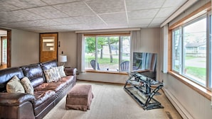 A living room with a leather couch, a TV, and a large window with a view of the outdoors. - National City Cottage w/ Patio, Steps to Lake! (National City)
