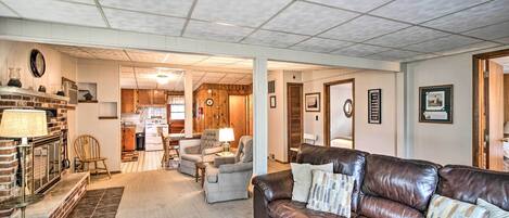 A spacious living room with a fireplace, a leather sofa, and a kitchen in the background.