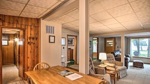 A spacious living area with a wooden dining table, comfortable seating, and a view of the outdoors through large windows. - National City Cottage w/ Patio, Steps to Lake! (National City)