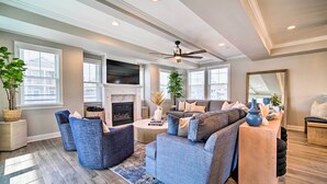 Un salon spacieux comprenant un canapé d’angle, deux fauteuils, une cheminée et un ventilateur de plafond.