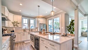 Une cuisine moderne avec des meubles blancs, un îlot central, des appareils en acier inoxydable et de grandes fenêtres offrant une vue dégagée.
