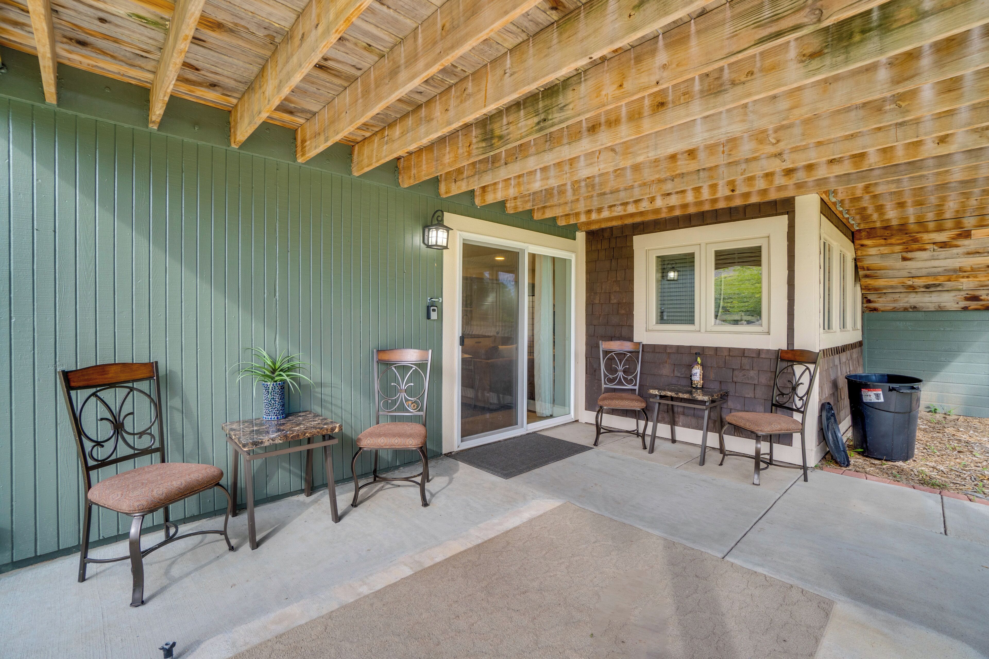An outdoor patio area with a covered seating area, a potted plant, and a trash can.