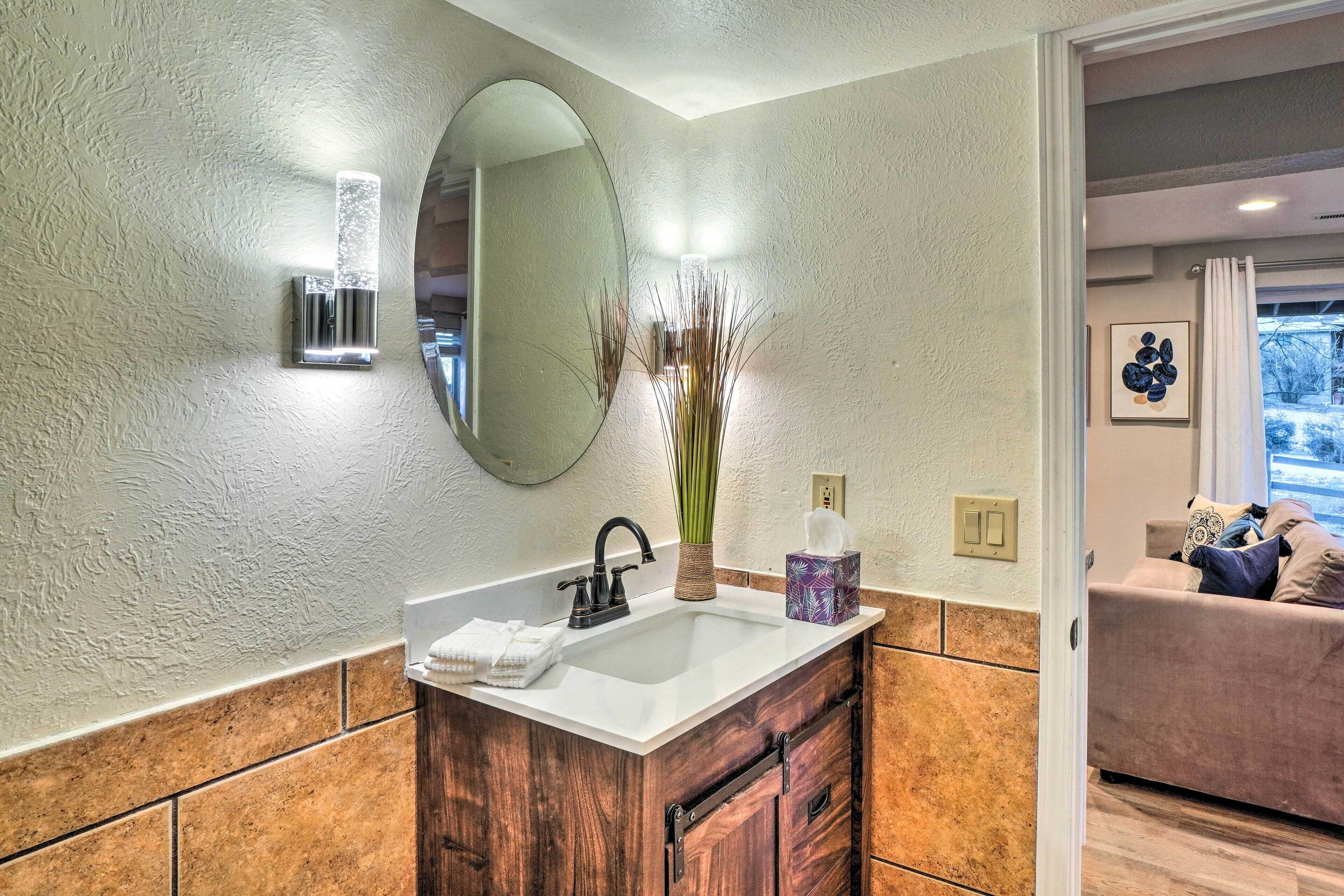 Une salle de bain avec un lavabo blanc, un meuble-lavabo en bois, un grand miroir et un vase contenant de hautes herbes.