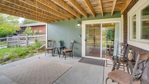 Une terrasse couverte avec un plafond en bois, une porte-fenêtre coulissante et une table avec des chaises.