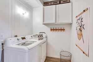 A laundry room with a front-loading washer and dryer, wooden cabinets, a hanging rack, and a basket.