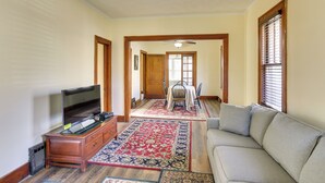 A living room with a sofa, TV, wooden cabinet, and a dining area with a table and chairs. - Quaint Omaha Home < 5 Mi to Downtown! (Omaha)