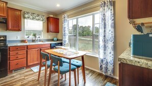 A kitchen with wooden cabinets, a granite countertop, a dining table with blue chairs, and a window with curtains. - Family Home in Rapid City ~ 4 Mi to Torch Lake! (Rapid City)
