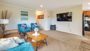 A living room with a brown leather sofa, blue armchairs, a wooden coffee table, and a TV mounted on the wall. - Family Home in Rapid City ~ 4 Mi to Torch Lake! (Rapid City)