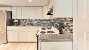 Et moderne køkken med hvide skabe, et rustfrit stål køleskab, en gasovn og et flisebeklædt backsplash.