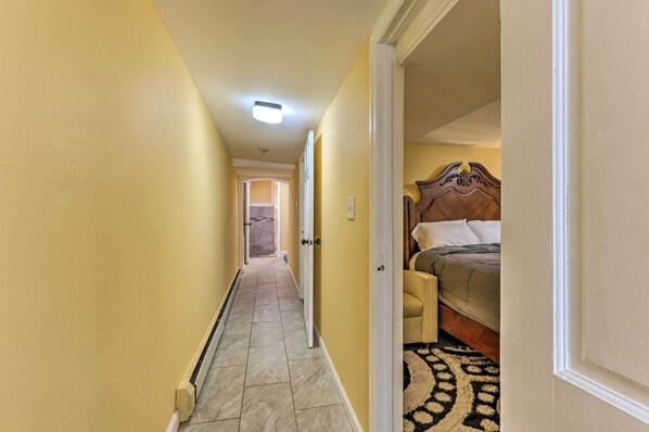 A narrow hallway with yellow walls and a tiled floor leading to a bedroom with a bed and a headboard.