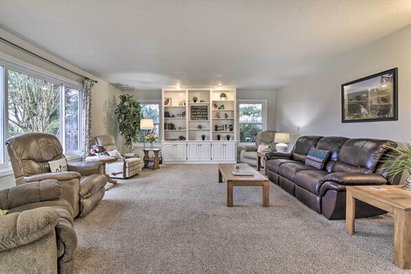 A living room with a beige carpet, a brown leather sofa, a brown leather armchair, a wooden coffee table, and a white entertainment unit with shelves. - Portland Area Home, 32 Mi to Mt Hood! (Boring)