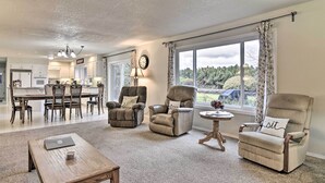 A spacious living room with a wooden coffee table, two armchairs, a dining area with a chandelier, and large windows with curtains. - Portland Area Home, 32 Mi to Mt Hood! (Boring)